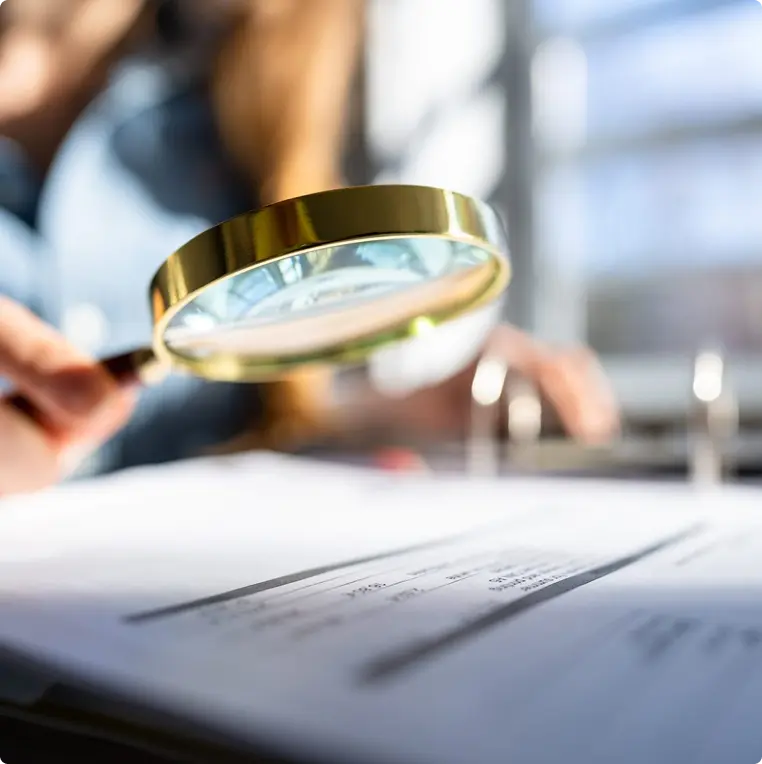 A woman's hand holds a magnifying glass over a document